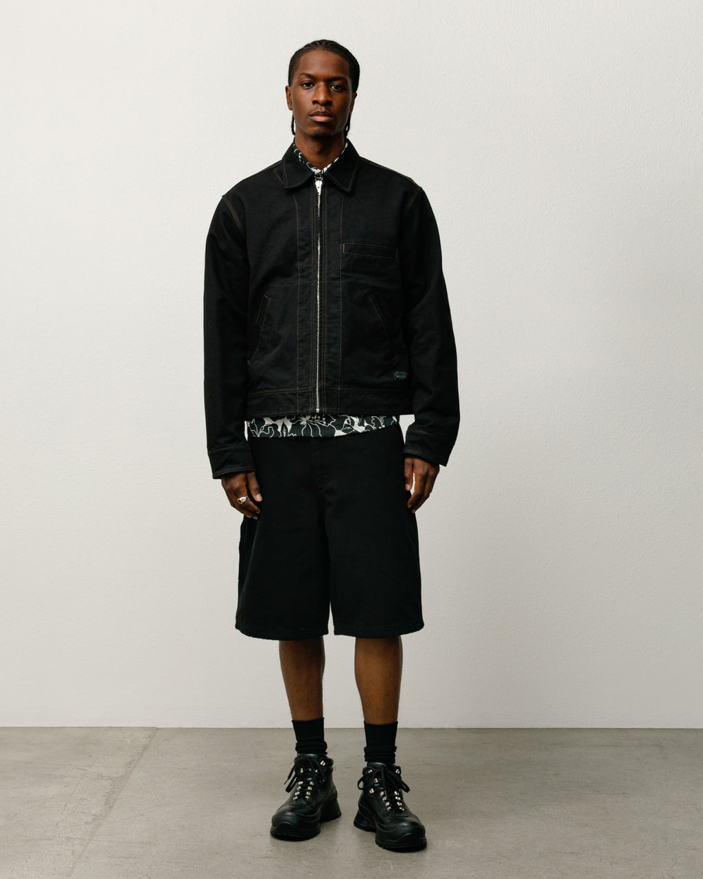 Person wearing a black jacket, shorts, and boots on a plain background.