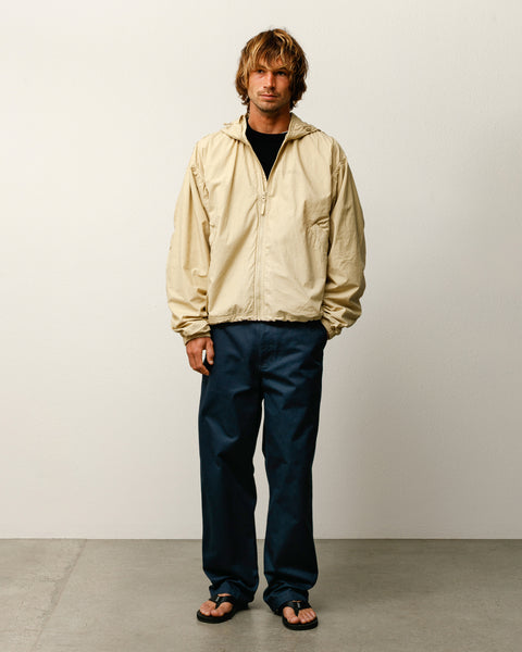 サンドカラーのStüssy Double Cotton Hooded Jacketアウターウェアを着用し、ネイビーのパンツとサンダルを合わせた男性モデルの全身ショット。