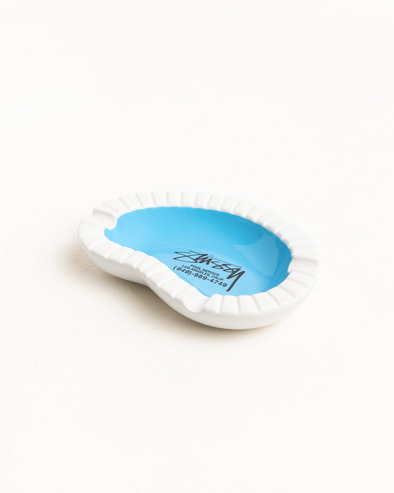 StüssyのPool Service Ashtray Accessories（マルチカラー）は、プールを模したセラミック製で、中央にブランドロゴがプリントされたユニークなデザインのアッシュトレイです。