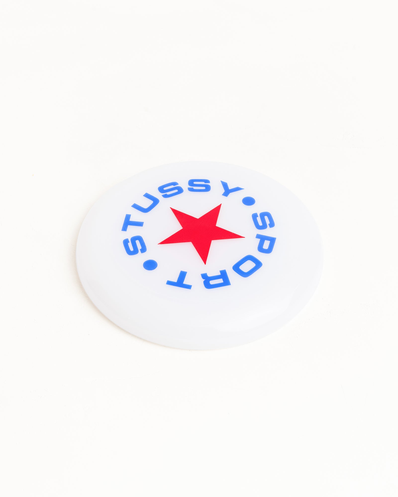 クリアカラーのStüssy Sport Frisbee Accessories。トップにはブルーのStüssyスポーツアートワークとレッドのスターがプリントされています。