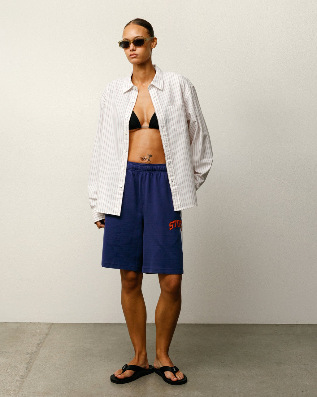 Person wearing a striped shirt, black bikini top, Stripe Jersey Short in Blue, and sunglasses against a plain background.